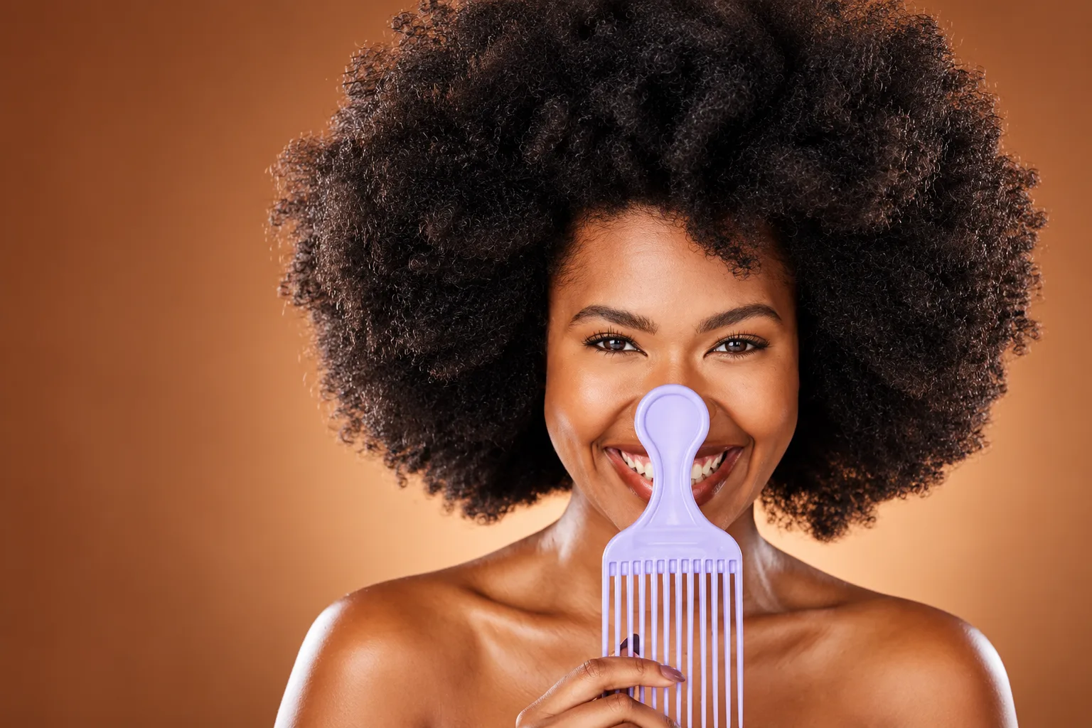 Mulher negra sorrindo, com cabelo black power volumoso, segurando um pente garfo