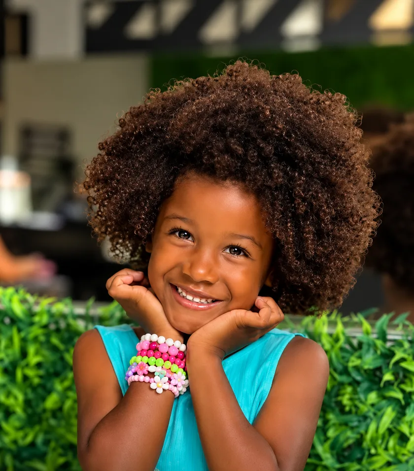 Menina sorrindo com o cabelo crespo finalizado, apoiando o rosto nas mãos